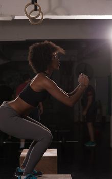 Fit young african american woman box jumping at a crossfit style gym. Female athlete is performing box jumps at gym.