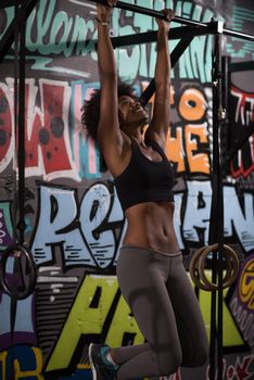 young beautiful african american woman athlete doing pull ups on the horizontal bar in the gym