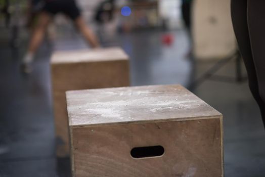 Fit young african american woman box jumping at a crossfit style gym. Female athlete is performing box jumps at gym with focus on legs