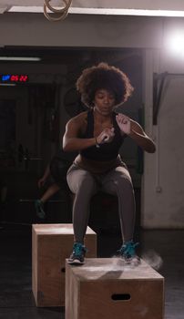 Fit young african american woman box jumping at a crossfit style gym. Female athlete is performing box jumps at gym.