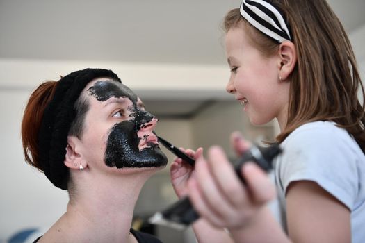 Family at home beauty treatment during coronavirus pandemic stay at home quarantine. Mother and little girl daughter  make a facial mask.