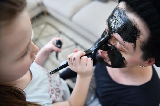 Family at home beauty treatment during coronavirus pandemic stay at home quarantine. Mother and little girl daughter  make a facial mask.