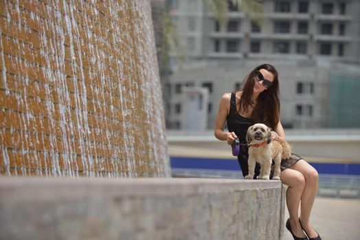 beautiful happy young  woman in black dress with cute small dog puppy have fun on street