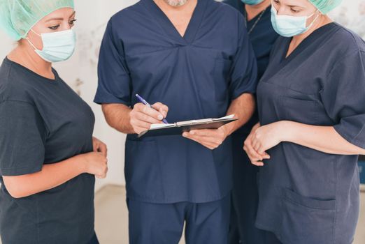 Orthopedic doctor in front of his medical multiethnic team wearing a face mask during covid-19 outbreak. Surgeon in front of his colleagues. Selective focus.