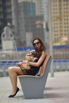 beautiful happy young  woman in black dress with cute small dog puppy have fun on street