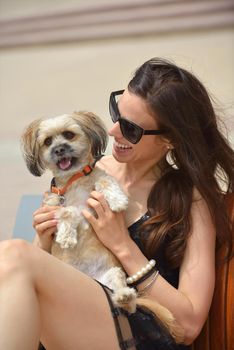 beautiful happy young  woman in black dress with cute small dog puppy have fun on street