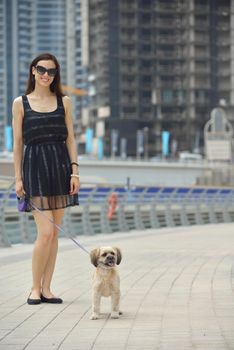 beautiful happy young  woman in black dress with cute small dog puppy have fun on street