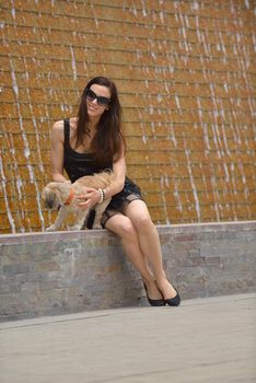 beautiful happy young  woman in black dress with cute small dog puppy have fun on street