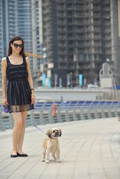 beautiful happy young  woman in black dress with cute small dog puppy have fun on street