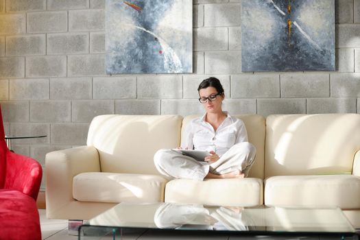 Young woman at home relaxing in her lliving room reading a digital tablet PC surf internet and work