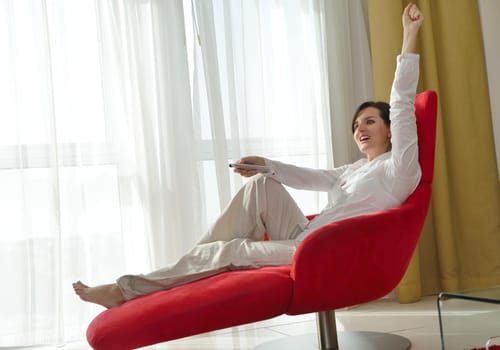 happy young woman relax at home on sofa in bright living room and watching tv