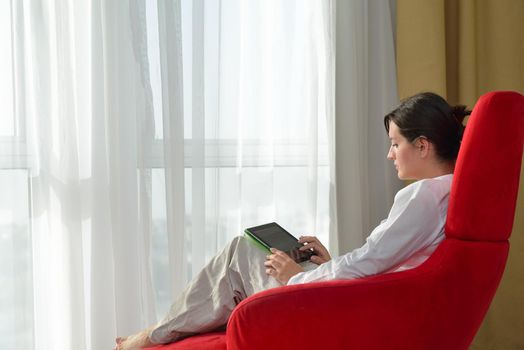 Young woman at home relaxing in her lliving room reading a digital tablet PC surf internet and work