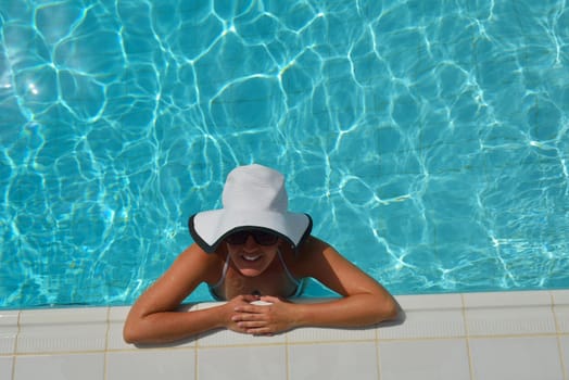 Happy smiling woman with hat and sunglasses  in swimming pool at tropical resort