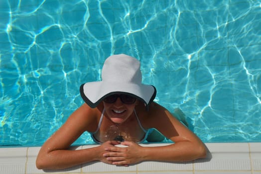 Happy smiling woman with hat and sunglasses  in swimming pool at tropical resort