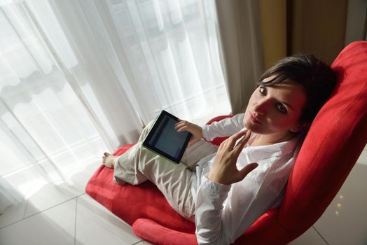 Young woman at home relaxing in her lliving room reading a digital tablet PC surf internet and work