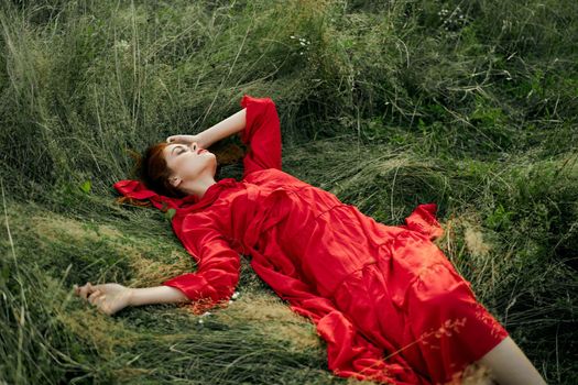 woman in red dress lies on the grass in the field nature landscape. High quality photo