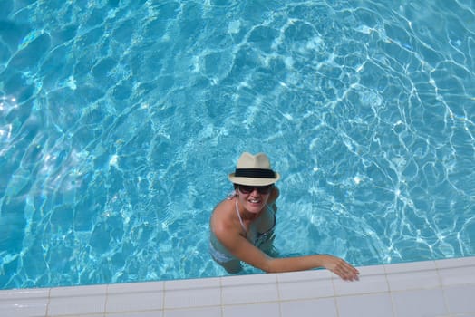 Happy smiling woman with hat and sunglasses  in swimming pool at tropical resort