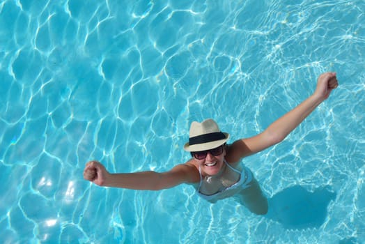 Happy smiling woman with hat and sunglasses  in swimming pool at tropical resort