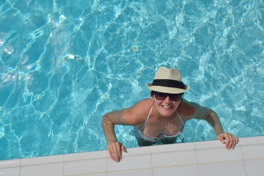 Happy smiling woman with hat and sunglasses  in swimming pool at tropical resort