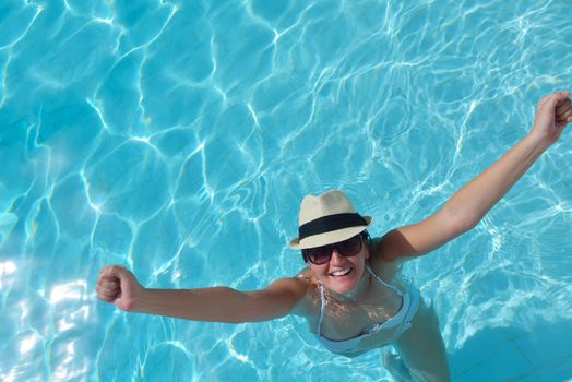 Happy smiling woman with hat and sunglasses  in swimming pool at tropical resort