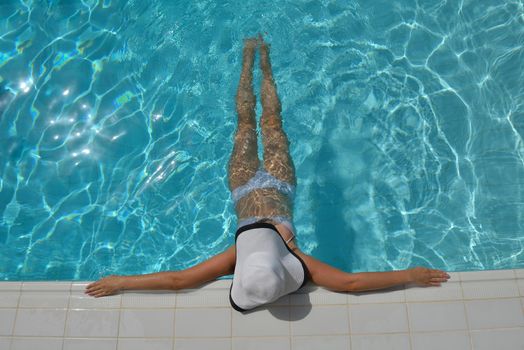 Happy smiling woman with hat and sunglasses  in swimming pool at tropical resort