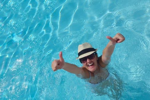 Happy smiling woman with hat and sunglasses  in swimming pool at tropical resort