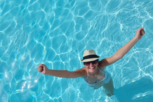 Happy smiling woman with hat and sunglasses  in swimming pool at tropical resort