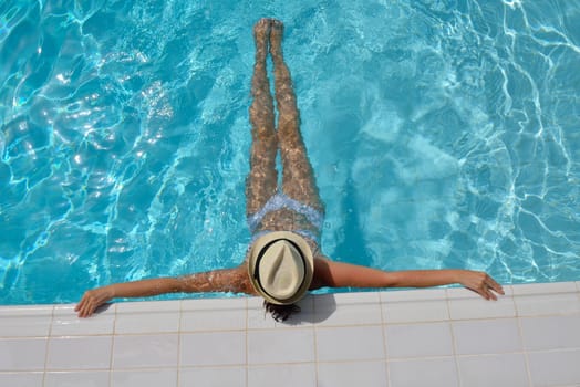 Happy smiling woman with hat and sunglasses  in swimming pool at tropical resort