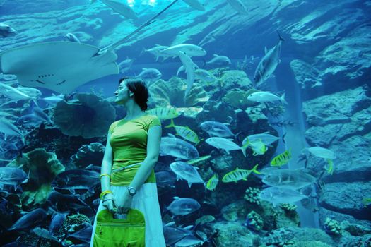 young woman  with big blue aquarium withmany  fish in background