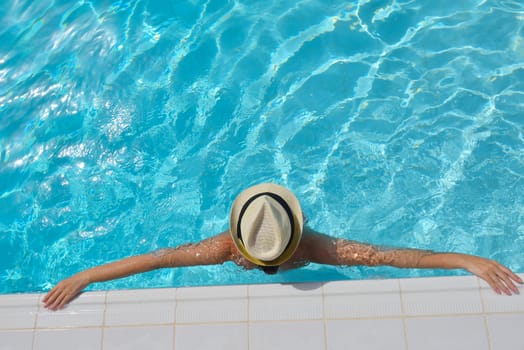 Happy smiling woman with hat and sunglasses  in swimming pool at tropical resort