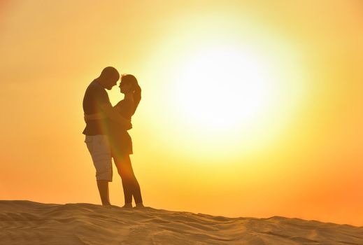 relaxed young pasionate couple enjoying the sunset  beauty on their honeymoon, on a desert with orange background