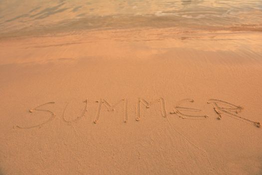 The Word Summer Written in the orange Sand background on a Beach at sunset