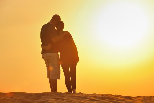 relaxed young pasionate couple enjoying the sunset  beauty on their honeymoon, on a desert with orange background