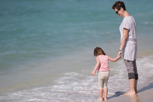 beautiful young mother and cute little girl are enjoying while running on exotic beach along the ocean Travel and Vacations.