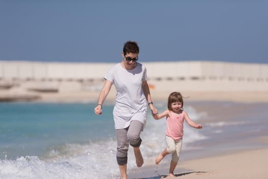 beautiful young mother and cute little girl are enjoying while running on exotic beach along the ocean Travel and Vacations.