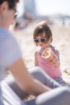 cool young mom and her little girl playing with a bucket full of sand wearing sunglasses and relaxing on the beach on a sunny day