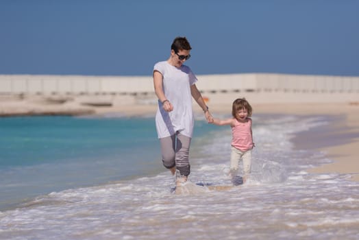 beautiful young mother and cute little girl are enjoying while running on exotic beach along the ocean Travel and Vacations.