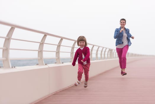 young mother and cute little girl running and cheerfully spend their time on the promenade by the sea