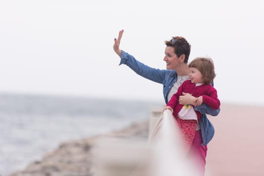 young mother and cute little girl running and cheerfully spend their time on the promenade by the sea