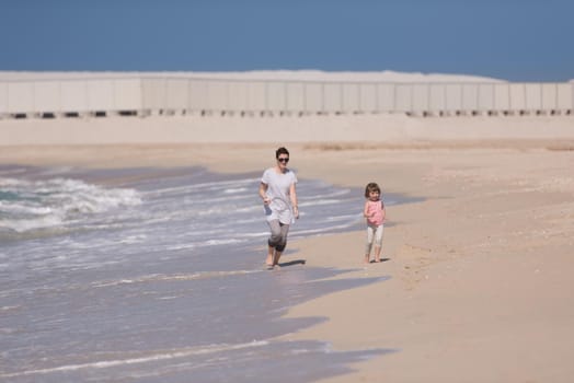 beautiful young mother and cute little girl are enjoying while running on exotic beach along the ocean Travel and Vacations.