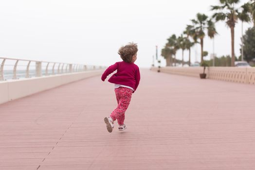 cute little girl running and cheerfully spend her time on the promenade by the sea