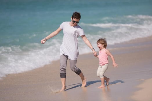 beautiful young mother and cute little girl are enjoying while running on exotic beach along the ocean Travel and Vacations.