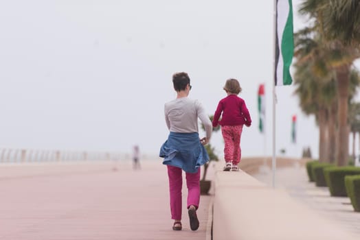 young mother and cute little girl running and cheerfully spend their time on the promenade by the sea