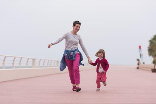 young mother and cute little girl running and cheerfully spend their time on the promenade by the sea