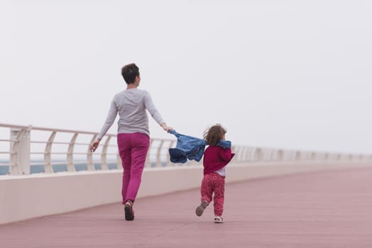 young mother and cute little girl running and cheerfully spend their time on the promenade by the sea