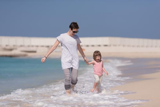 beautiful young mother and cute little girl are enjoying while running on exotic beach along the ocean Travel and Vacations.