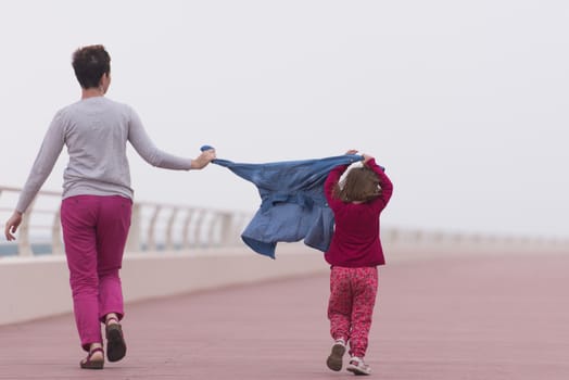 young mother and cute little girl running and cheerfully spend their time on the promenade by the sea