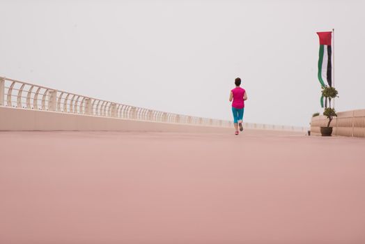 very active young beautiful woman busy running on the promenade along the ocean side to keep up her fitness levels as much as possible