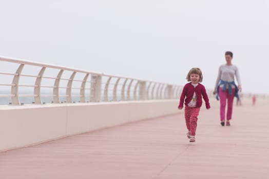 young mother and cute little girl running and cheerfully spend their time on the promenade by the sea