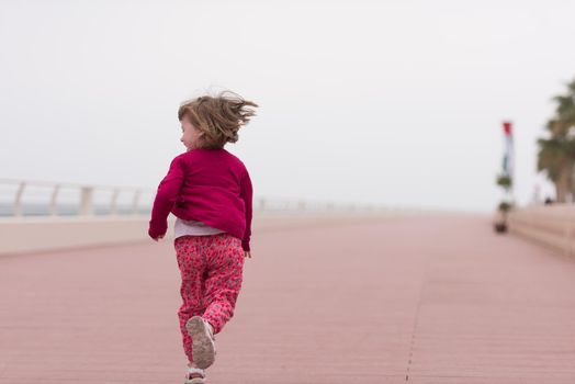 cute little girl running and cheerfully spend her time on the promenade by the sea